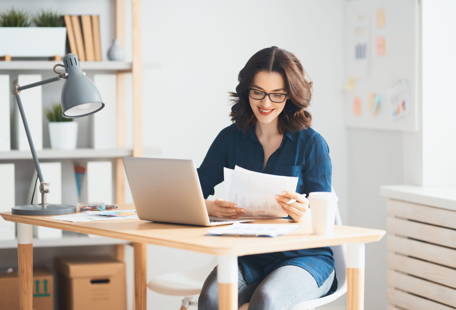 a woman on her laptop, looking at some paper files next to the laptop 
